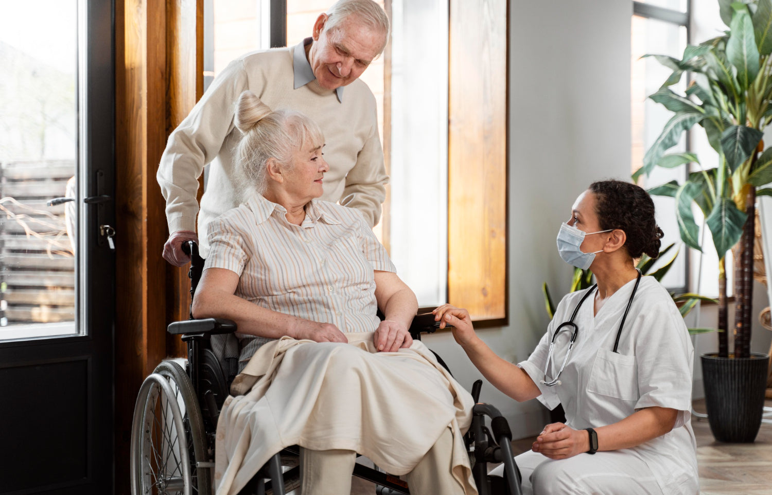 Pflegender Angehöriger mit Ehefrau im Rollstuhl im Arztgespräch